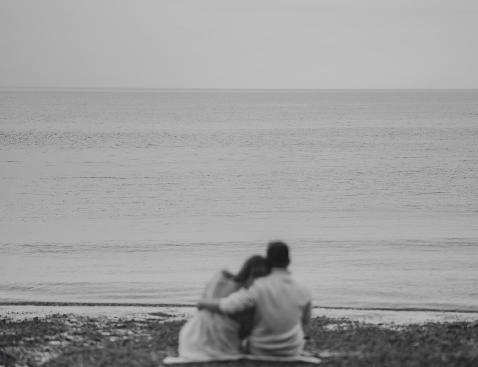 A couple sitting close together by the sea during their engagement shoot